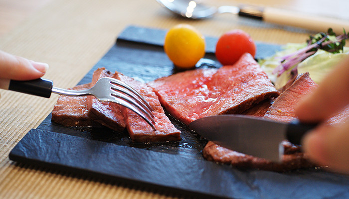 A woman is cutting roast beef with Japanese cutlery