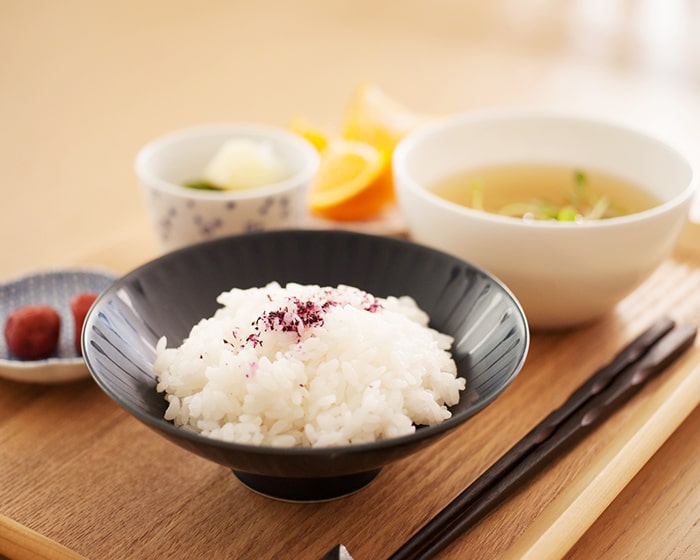 ネイビーマットの平茶碗にごはんが盛られている食卓