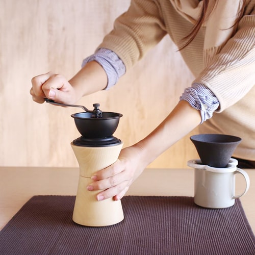 A woman grinds coffee beans with Japanese coffee grinder from MokuNeji