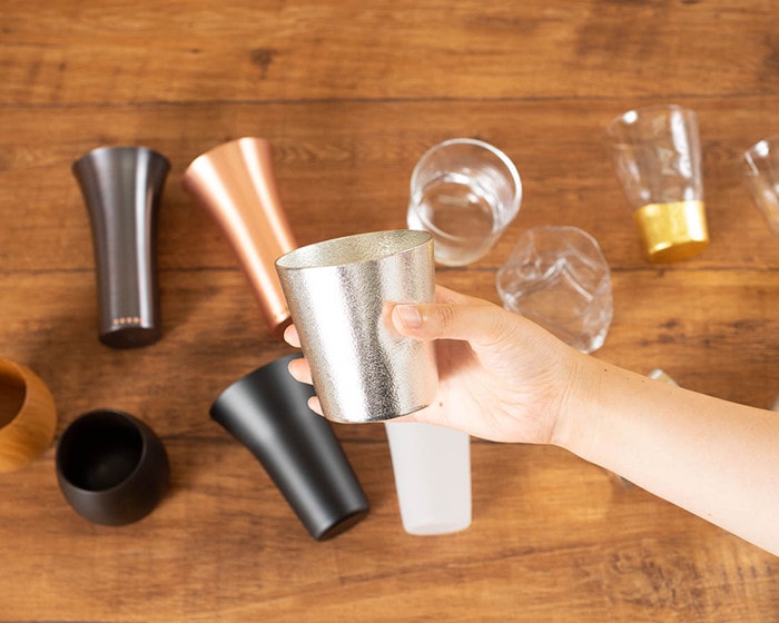 Various whiskey cups and tumblers on the table and a woman has tin tumbler from Nousaku